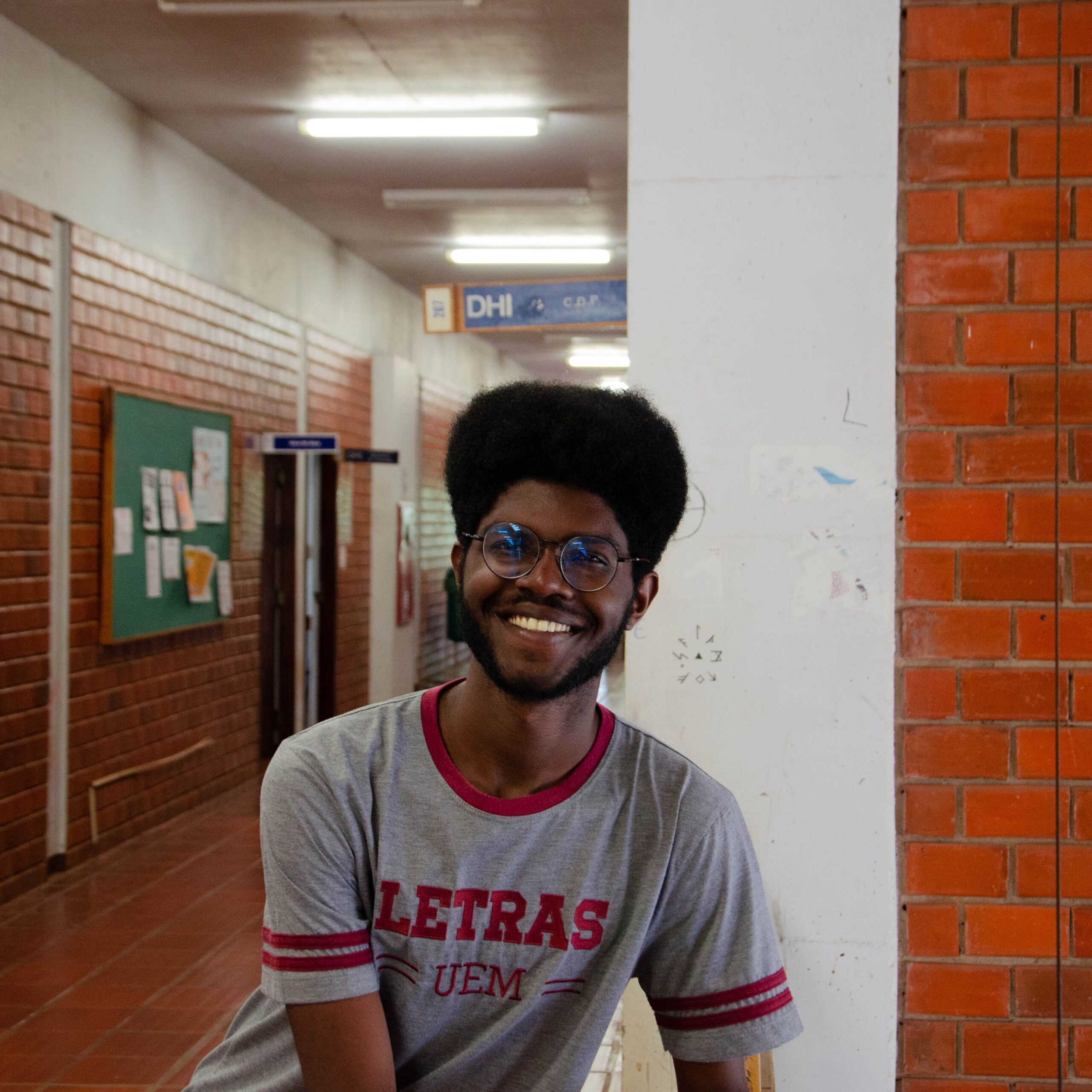 Cheerful student with glasses leaning in a university hallway at day.