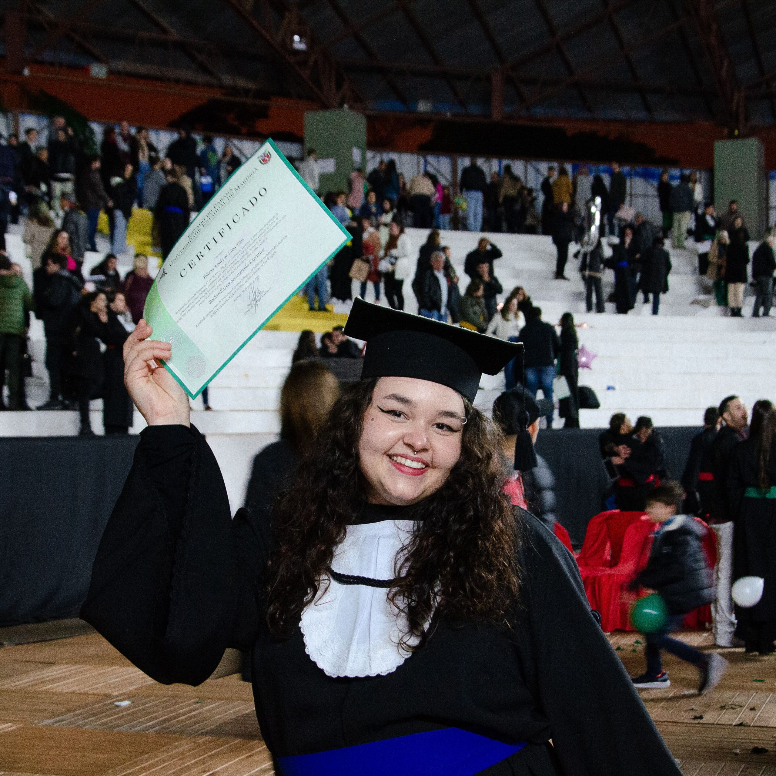 Smiling female graduate celebrating with certificate indoors at graduation ceremony.